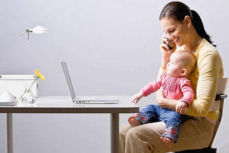 Working mother holding baby while talking on cell phone at desk